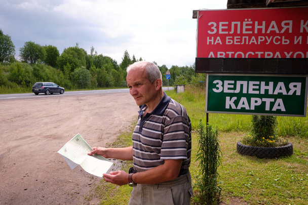 Pskov region. Russia - July 5, 2018: Point of sale of green car cards and insurance CTP on the border with the Republic of Belarus. Man examines insurance documents. - Zdjęcie, obraz