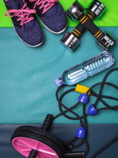 Sportaccessoires von oben. Damensneakers, Wasserflasche, Expander, Pressrolle auf grüner Matte, Kopierraum - Foto, Bild