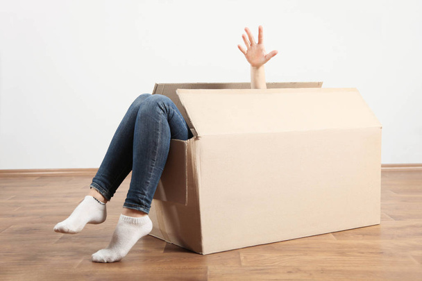 Boîte en carton avec pieds femelles se tient sur le sol en bois dans la chambre. Concept déménagement dans un nouvel appartement, colis. Espace de copie
. - Photo, image
