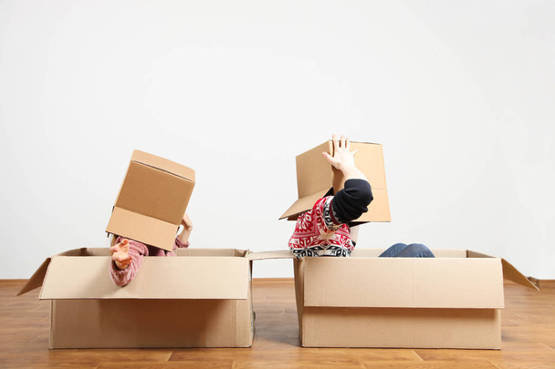Парень и девочка, молодая веселая пара с коробками на голове сидят в коробках в новой квартире. Концепция переезда, покупки квартиры, ремонта. Копирование пространства
. - Фото, изображение