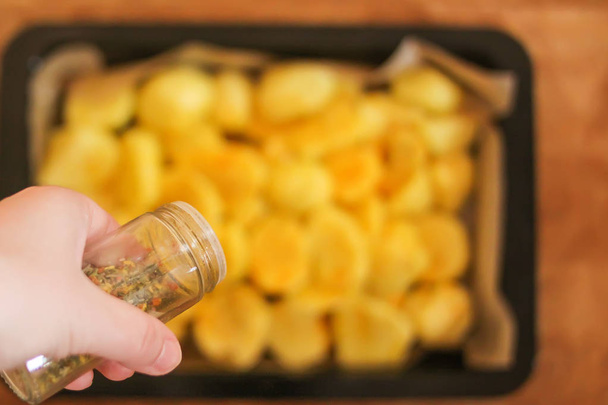 Raw potatoes prepared for baking with flavorings on tray. - Valokuva, kuva