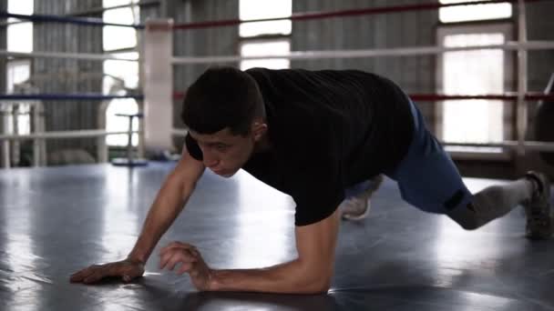 Крупным планом молодой мускулистый спортсмен делает отжимания - от локтей до протянутых рук - во время тренировки в боксерском зале
 - Кадры, видео