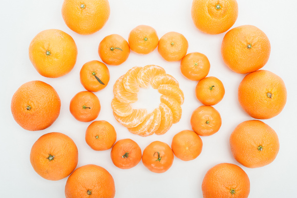 flache Lage mit Kreisen aus geschälten Mandarinenscheiben und ganzen Mandarinen auf weißem Hintergrund - Foto, Bild