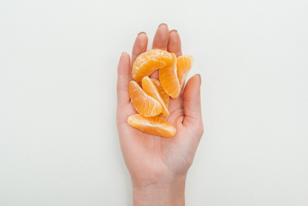 částečný pohled ženy držící oloupaná mandarinka plátky na bílém pozadí - Fotografie, Obrázek