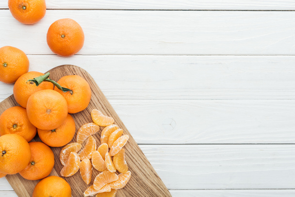 сверху вид на очищенные мандариновые ломтики и целые спелые мандарины на деревянной доске
  - Фото, изображение