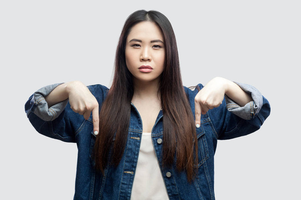 hopeful beautiful brunette asian young woman in casual blue denim jacket with makeup standing with crossed fingers and praying on light grey background. - Foto, Imagen