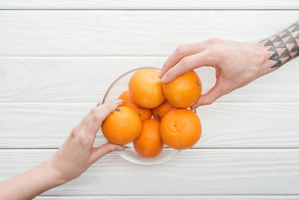 vue recadrée d'un homme et d'une femme tatoués prenant des mandarines dans un bol en verre
 - Photo, image