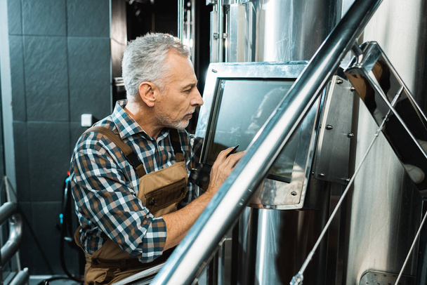 professional male brewer looking at screen of brewery equipment - Photo, Image