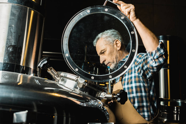 professionele mannelijke brouwer in werkende Amerikaanse overalls brouwerij apparatuur controleren - Foto, afbeelding