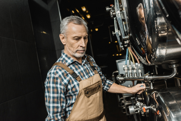 professionele mannelijke brouwer in overalls werken met brouwerij apparatuur - Foto, afbeelding