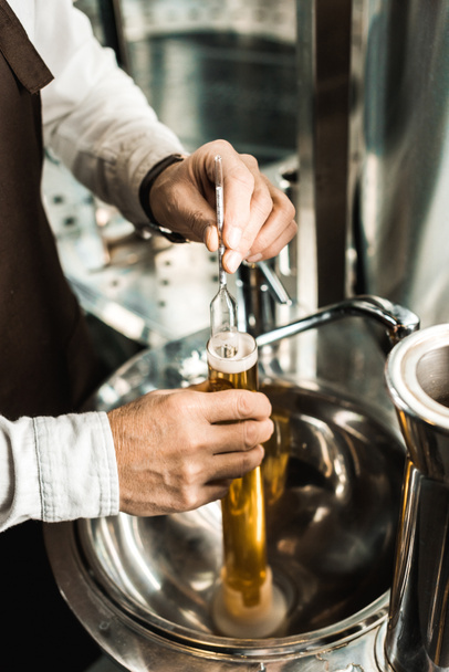 cropped view of male brewer examining beer in flask in brewery - Фото, зображення