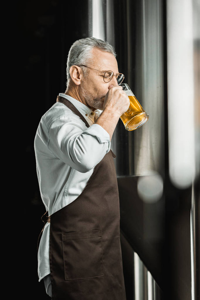 schöner männlicher Brauer trinkt Bier aus Glas in Brauerei - Foto, Bild