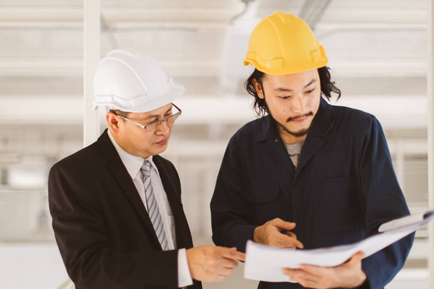 Asian executive engineer and young engineer look at blueprint and discuss together, concept for engineer in industrial factory. - Photo, Image