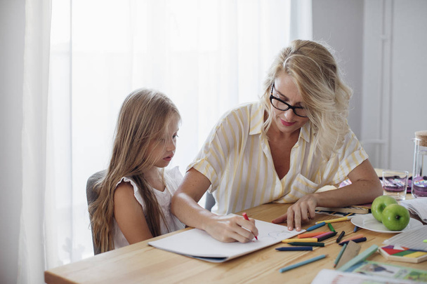 Cute blonde Caucasian girl writing with her mother helping. - Фото, зображення