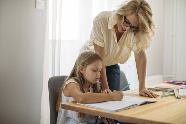Beautiful blonde Caucasian woman helping to her cute daughter to study at home. - Foto, Bild