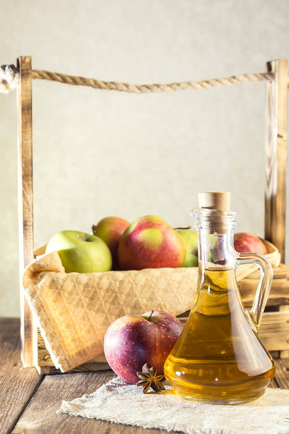 Processing of an agricultural crop of red and green apples. Homemade preparations, healthy diet vegetarian food. Spiced apple cider vinegar, juice, cider in a glass jug next to a box of ripe fruit - Φωτογραφία, εικόνα