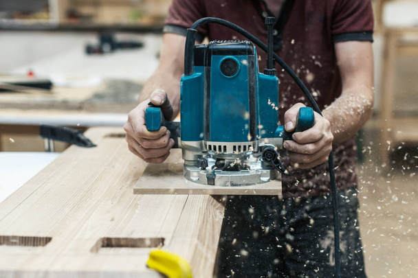 manuelles Holzkonzept. beschnitten Nahaufnahme Foto von Schreiner Handwerker mit elektrischem Werkzeug in den Händen machen Möbel in Garage oder Arbeitszimmer - Foto, Bild