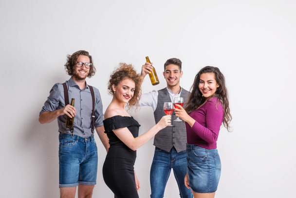 Πορτρέτο του ομάδα νεαρών, των φίλων, στέκεται σε ένα στούντιο, κρατώντας μπουκάλια και ποτήρια. - Φωτογραφία, εικόνα