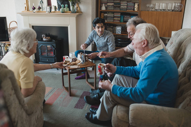 Teenage boy is assisting senior adults having a tea party at a nursing home. - 写真・画像