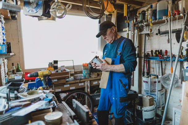 Senior man is working in his shed and is reading the label on a varnish. - Fotoğraf, Görsel