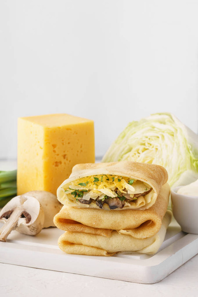 Stack of vegetarian crepes or blintzes with cabbage, mushrooms and cheese filling and ingredients for cooking. - Фото, зображення