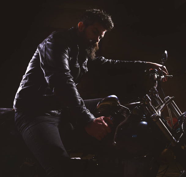 Macho, brutal biker in leather jacket riding motorcycle at night time, copy space. Night racer concept. Man with beard, biker in leather jacket sitting on motor bike in darkness, black background - Photo, image