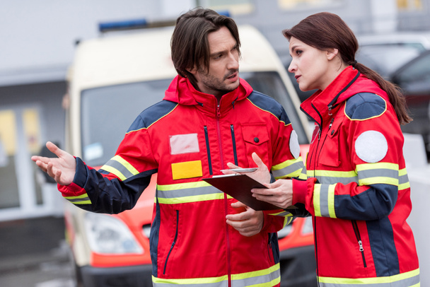 Paramedici in uniforme rossa con appunti che parlano in strada
 - Foto, immagini