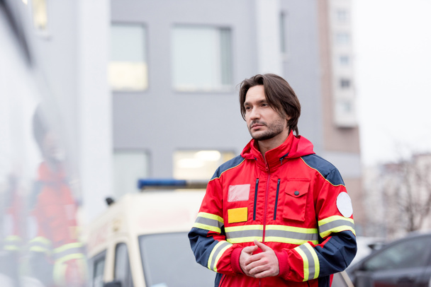 Pensive paramedic in red uniform standing on street - Foto, imagen