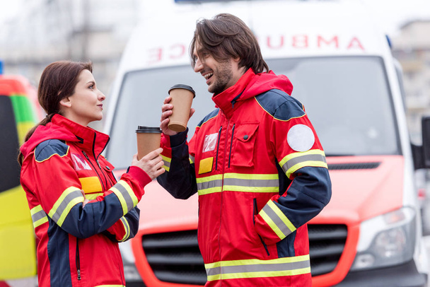 Paramédicos sonrientes tomando café frente al coche de la ambulancia
 - Foto, Imagen