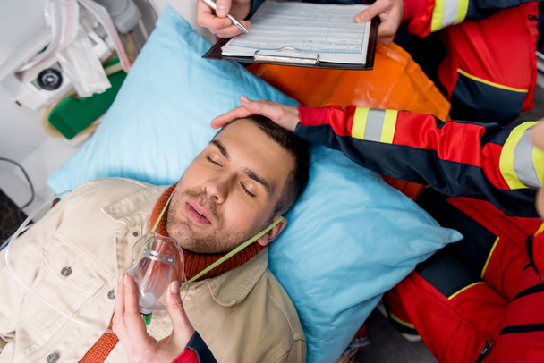 Vista cortada de paramédico colocando máscara de oxigênio no paciente inconsciente
 - Foto, Imagem