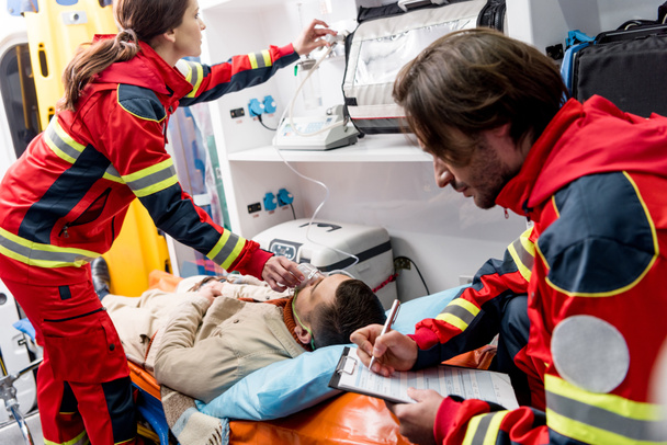 Záchranáře v schránky zatímco kolega drží kyslíkovou masku na pacienta - Fotografie, Obrázek