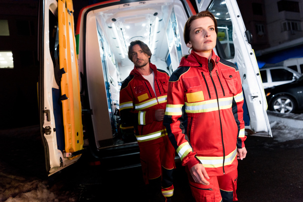 Sanitäter in roter Uniform stehen neben Rettungswagen - Foto, Bild