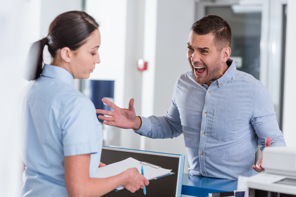 Агрессивный мужчина кричит на медсестру в клинике
 - Фото, изображение