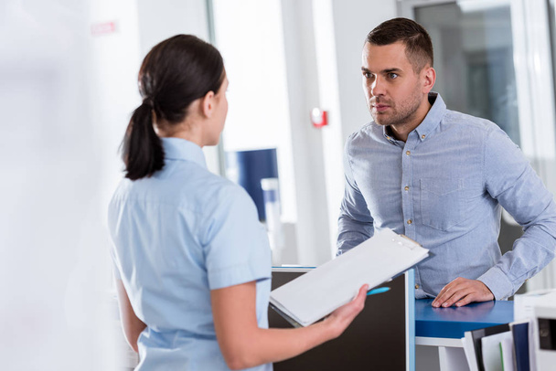 Пациент в синей рубашке слушает медсестру в клинике
 - Фото, изображение