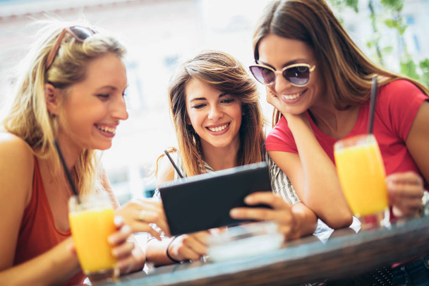 Three beautiful friends in a cafe using tablet pc and having fun - Foto, imagen