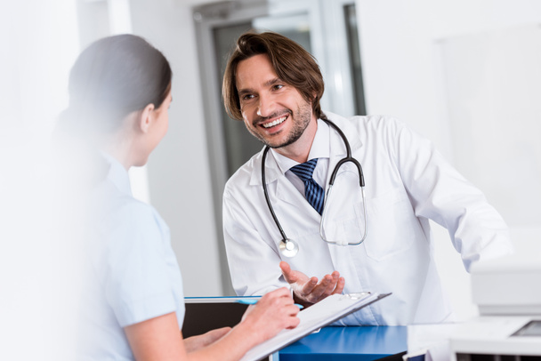 Smiling doctor with stethoscope talking to nurse - Photo, Image