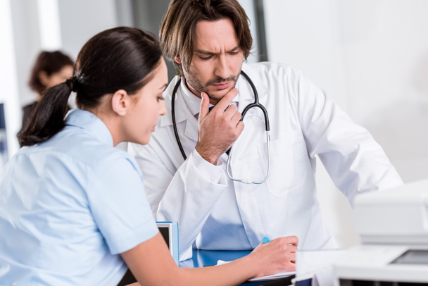 Serious doctor in white coat talking to nurse in clinic - Foto, Imagen