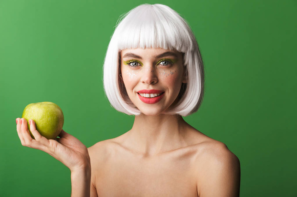 魅力的な若いトップレス女性短い白髪立っている緑の背景の上分離された身に着けているリンゴを表示 - 写真・画像