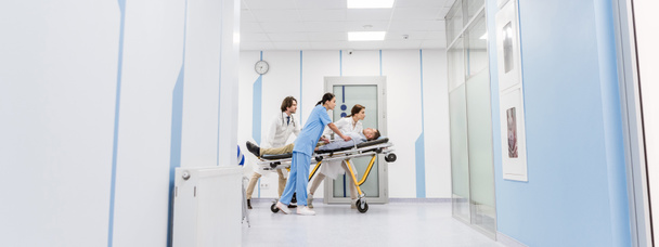 Médicos y enfermeras concentrados transportando a un paciente inconsciente en camilla
  - Foto, imagen