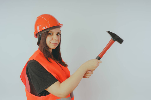 Girl Builder with hammer in hand, concept: girl doing repairs. A woman in a helmet and an orange vest, in the image of a road worker or surveyor - Foto, immagini