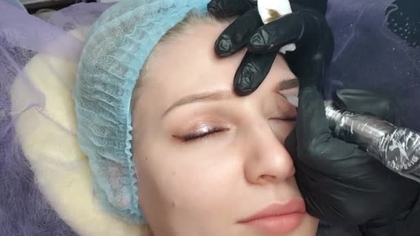 mooie blue-eyed blonde doet permanente make-up wenkbrauwen in een schoonheidssalon, close-up - Video