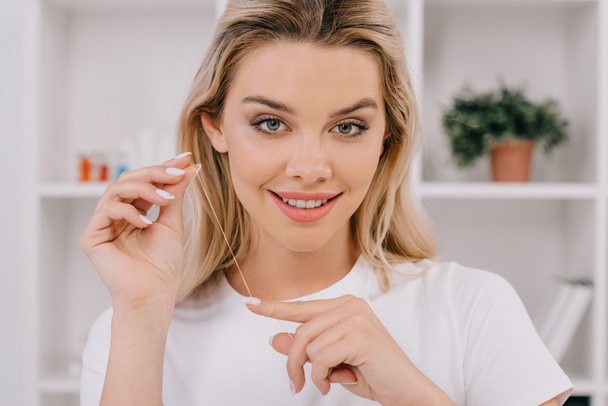 beautiful smiling woman holding dental floss and looking at camera - Fotoğraf, Görsel