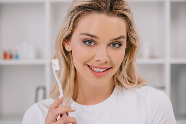 beautiful smiling woman holding toothbrush and looking at camera - Fotografie, Obrázek