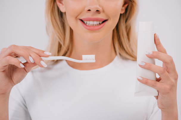 vista recortada de la mujer sonriente sosteniendo cepillo de dientes y pasta de dientes con espacio de copia aislado en blanco
 - Foto, Imagen