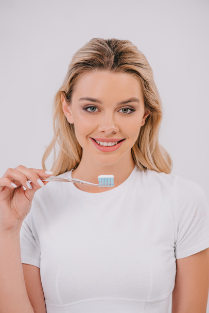 όμορφη χαμογελαστή γυναίκα εκμετάλλευση οδοντόβουρτσα και βλέπουν τα φωτογραφικών μηχανών που απομονώνονται σε λευκό - Φωτογραφία, εικόνα