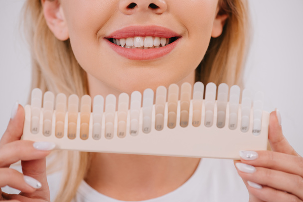 vista recortada de la mujer sonriente sosteniendo dientes paleta de colores aislado en blanco, dientes concepto de blanqueamiento
 - Foto, imagen