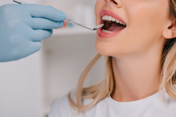 vista parziale del dentista esaminando i denti della giovane donna con specchio bocca
 - Foto, immagini