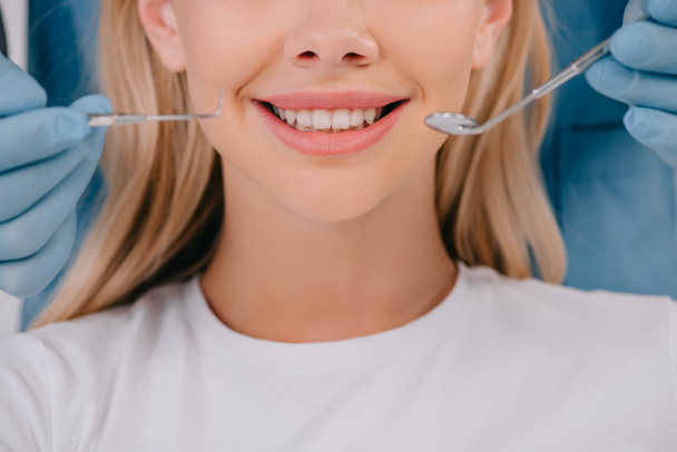 vista recortada del dentista sosteniendo el espejo de la boca y la sonda dental cerca de la mujer sonriente
 - Foto, Imagen