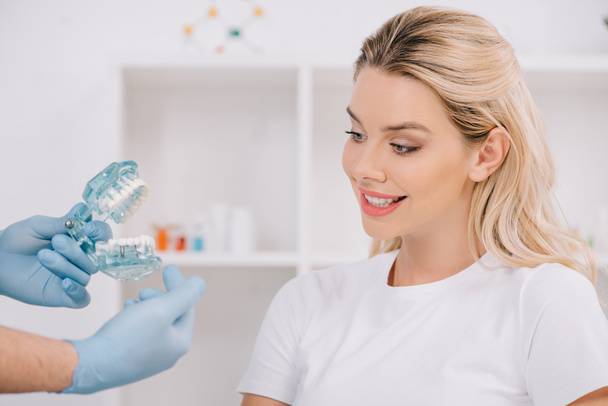 mooie lachende vrouw kijken orthodontist kaak model houden tijdens overleg in kliniek - Foto, afbeelding