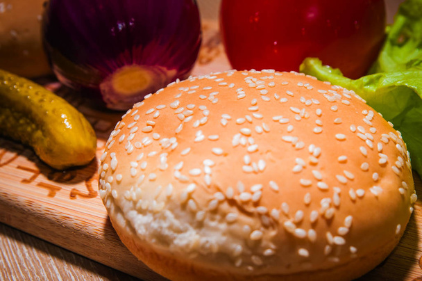 Red tomato, purple onion, green lettuce, pickled cucumber and bun on wooden background. - Foto, Bild